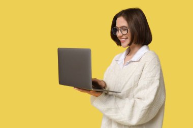 Sarı arka planda modern dizüstü bilgisayarla çalışan güzel genç bir kadın.