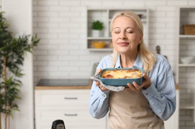 Güzel olgun bir kadın mutfakta lezzetli lazanyayla fırın tabağı tutuyor.