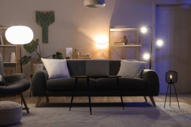 Karanlık oturma odasının içinde siyah kanepe ve geceleri parlayan lambalar.