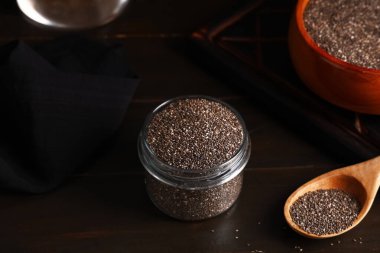 Ahşap zemin üzerinde chia tohumları olan kavanoz ve kaşık.