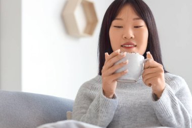 Evde bir fincan kakaolu genç Asyalı kadın, yakın plan.