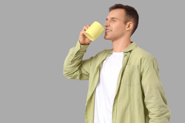 Genç adam gri arka planda sıcak çay içiyor.