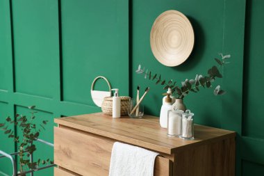 Okaliptüs dallı vazo ve kozmetik ürünleri banyodaki yeşil duvarın yanındaki çekmecelerde.