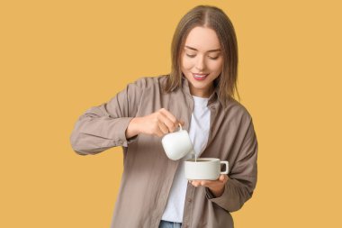 Güzel genç bir kadın sürahide taze süt dolduruyor sarı arka planda sıcak bir kahveye.