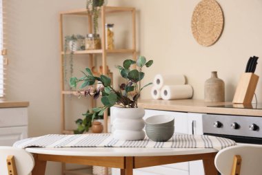 Mutfaktaki yemek masasında okaliptüs dalları ve tabakları olan vazo.