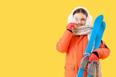 Sarı arka planda kayak ve kar taneleri olan kalın elbiseli tatlı bir kız.