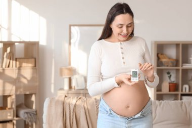 Genç hamile kadın evde glukometre kullanıyor. Gebelik Diyabet Konsepti