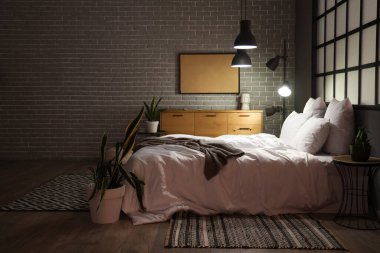 Geceleri rahat yatağı ve parlak lambaları olan modern yatak odasının içinde.