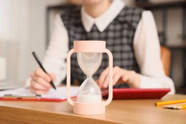 Ofiste çalışan iş kadınına karşı masaya pembe kum saati, yakın plan.