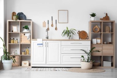 Beyaz tezgahlı, çatal bıçaklı ve raflı şık mutfak.