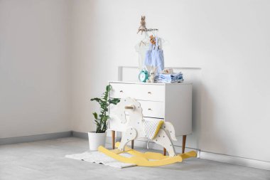 Şık çocuk odasının içinde sallanan at, elbise ve bebek kıyafetleri ışık duvarında asılı.