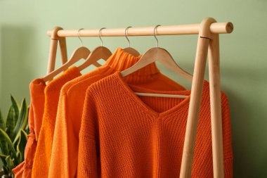 Yeşil duvarın yanında parlak turuncu elbiseli raflar, yakın plan