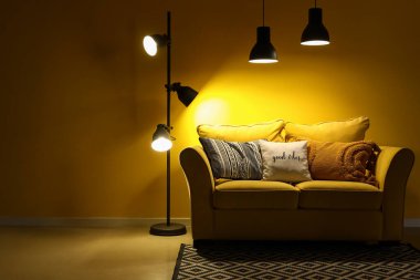 Şık oturma odasının içinde rahat sarı kanepe ve geceleri parlayan lambalar.