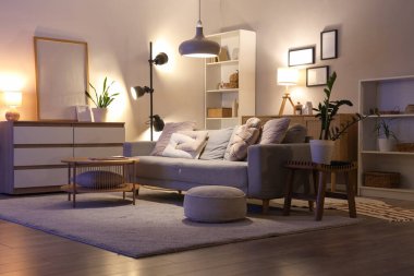 Oturma odasının içinde kanepe, raf ünitesi ve akşam lambaları var.