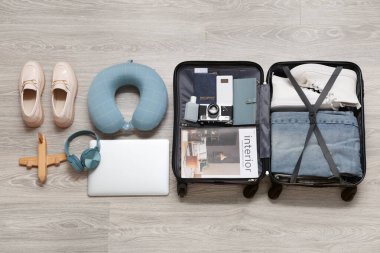 Seyahat aksesuarları ve gri ahşap zeminde modern aletlerle dolu bavul.