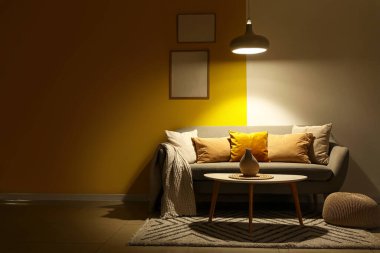 Gri kanepesi, masası ve parlayan lambası olan karanlık oturma odasının içinde.