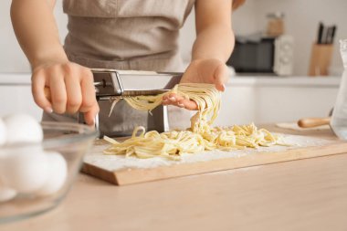 Mutfaktaki masada makineyle makarna yapan genç kadın, yakın plan.