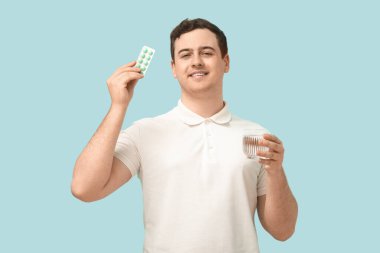 Haplardan su toplayan ve mavi arka planda bir bardak suyu olan mutlu genç adam.