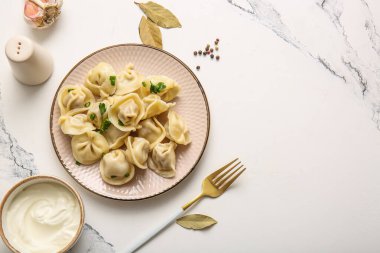 Maydanozlu kaynamış hamur köftesi ve beyaz arka planda bir kase ekşi krema.