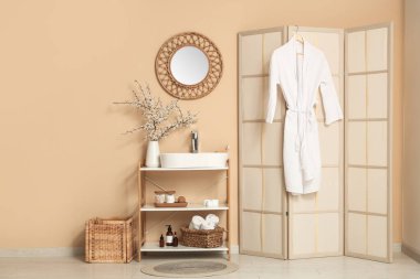 Çiçek açan dallı vazo ve banyonun içindeki bej duvarın yanında lavabo.