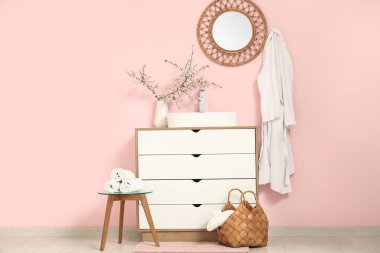 Banyonun içinde, pembe duvarın yanındaki çekmecelerin üstündeki vazoda çiçek açan dallar var.