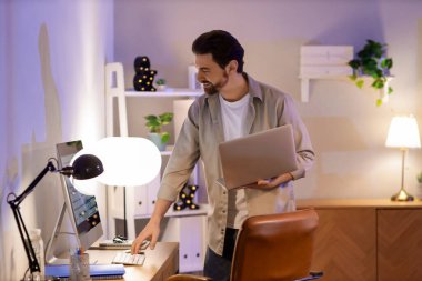 Genç adam akşam ofiste dizüstü bilgisayar ile çalışıyor.