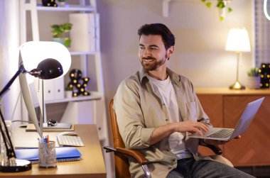 Genç adam akşam ofiste dizüstü bilgisayarla çalışıyor.