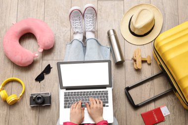 Üst katta seyahat aksesuarları olan dizüstü bilgisayar kullanan bir kadın.