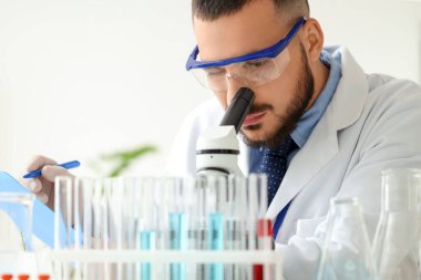 Güvenlik gözlüklü erkek bilim adamı laboratuvarda mikroskoptan bakıyor, yakın plan.