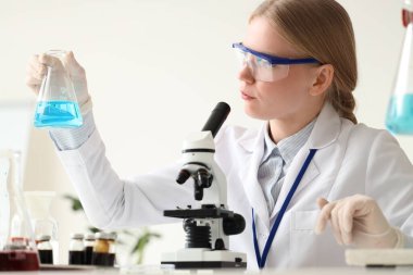 Matarası ve mikroskobu olan kadın bilim adamı laboratuarda çalışıyor.