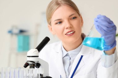 Laboratuvarda kimyasal matarası ve mikroskobu olan kadın bilim adamı.