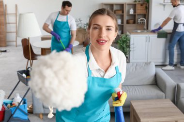 Odada deterjan ve toz bezi olan genç bir kadın hademe var.