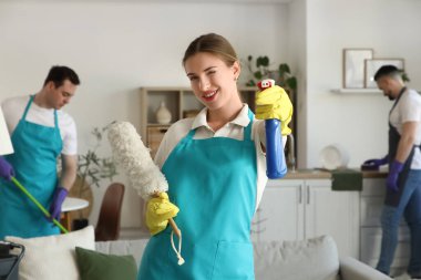 Odada deterjan ve toz bezi olan genç bir kadın hademe var.