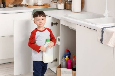 Mutfaktaki açık çekmecenin yanında deterjanı olan küçük bir çocuk. Tehlikedeki çocuk