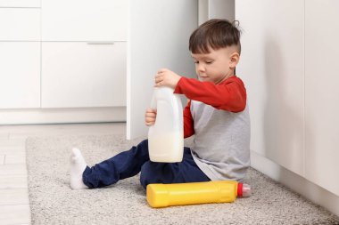 Küçük çocuk mutfakta bir şişe deterjan açıyor. Tehlikedeki çocuk