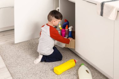 Küçük çocuk mutfak çekmecesinden temizlik malzemesi alıyor. Tehlikedeki çocuk