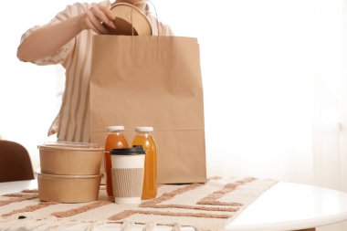 Genç bir kadın mutfaktaki masadaki kese kağıdından konteynır alıyor. Yemek dağıtım servisi.