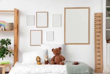 Raf üniteli çocuk odasının içi, ahşap stadyum ölçer, boş çerçeveler ve yatakta oyuncaklar.