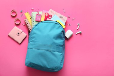 Mavi okul çantası, farklı kırtasiye malzemeleri ve pembe arka planda modern kulaklıklar.