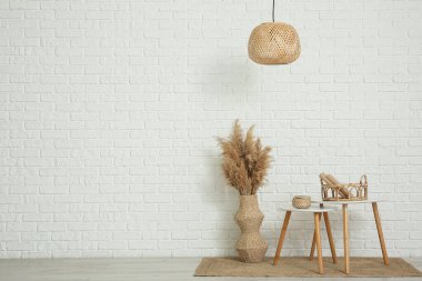 Kahve masaları ve vazo, odanın içinde beyaz tuğla duvarın yanında çimen var.