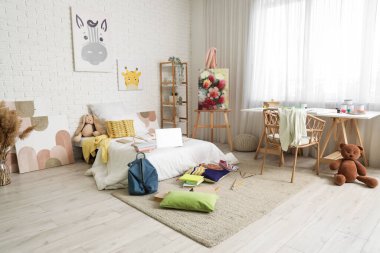 İçinde yatak, sehpa ve masa olan dağınık çocuk odası.