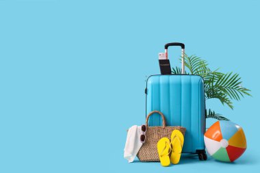 Mavi arka planda plaj aksesuarlarıyla dolu bavul.