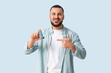 Genç adam arka plandaki astım spreyini işaret ediyor.