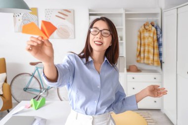 Evinde kağıttan uçağı olan Asyalı genç bir iş kadını.