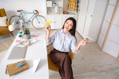 Evinde kağıt uçağı olan genç bir iş kadını.