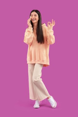 Genç bir kadın menekşe arka planında iyi görünüyor ve cep telefonuyla konuşuyor