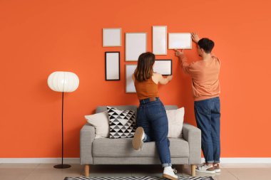Evdeki turuncu duvara boş çerçeveler asan genç bir çift.