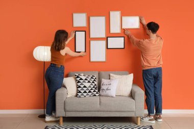 Evdeki turuncu duvara boş çerçeveler asan genç bir çift.