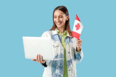 Kanada bayrağı taşıyan genç bir kadın mavi arka planda dizüstü bilgisayar kullanıyor