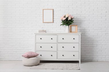 Pouf, çekmece ve vazo. Odanın içinde güzel şakayık çiçekleri var.